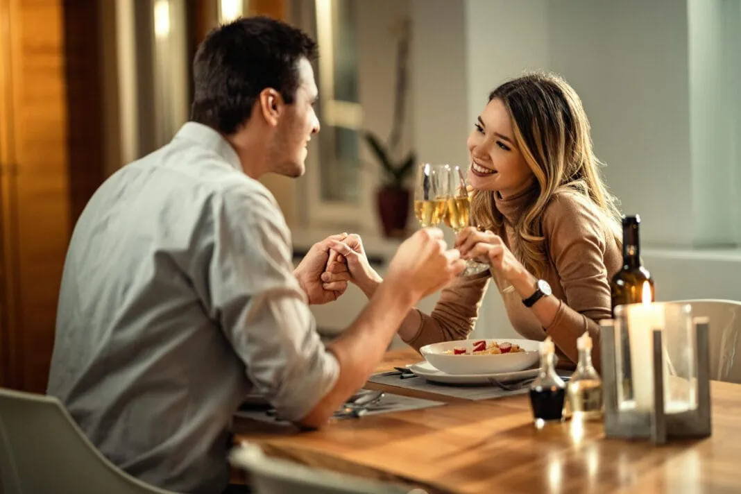 happy-woman-her-boyfriend-holding-hands-while-toasting-with-champagne-while-having-dinner-dining-table